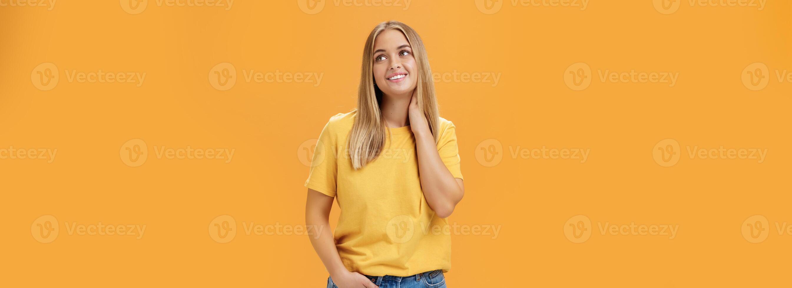 bella e tenero carino europeo femmina indipendente libero professionista nel giallo maglietta sospiri toccante collo e guardando sognante a superiore giusto angolo con piacevole Sorridi, in posa al di sopra di arancia sfondo foto