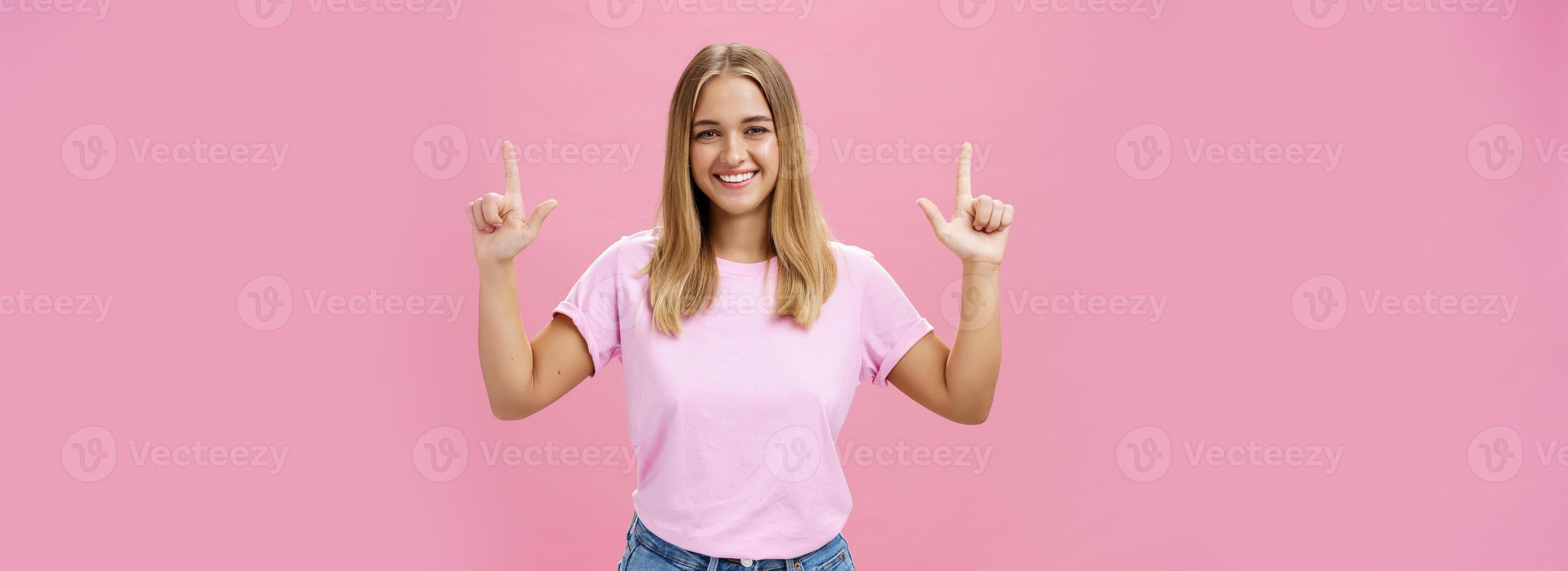 interno tiro di piacevole attraente dall'aspetto amichevole ragazza con abbronzato pelle nel casuale maglietta e jeans raccolta mani puntamento su e sorridente a grandi linee a telecamera con soddisfatto Guarda al di sopra di rosa sfondo foto