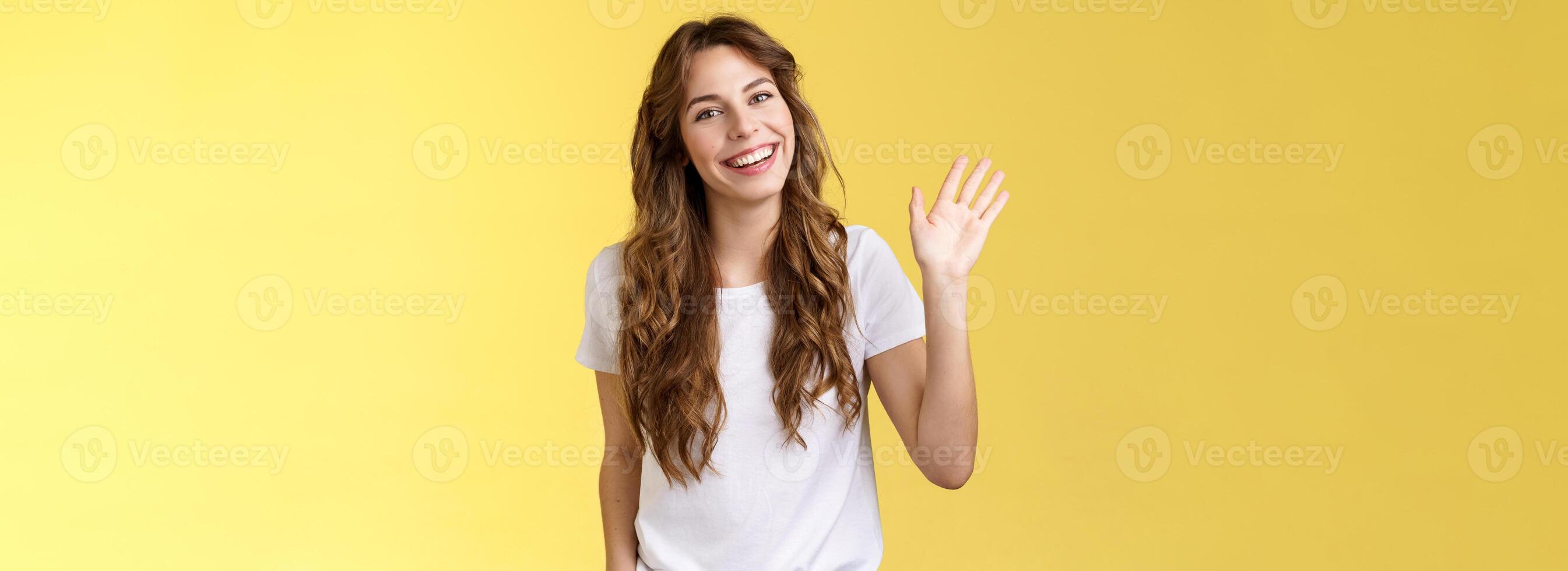 modesto carino amichevole estroverso attraente europeo donna lungo Riccio taglio di capelli agitando palma socievole conversazione introdurre se stessa sorridente a grandi linee dire Ciao Ciao saluto collaboratore giallo sfondo foto