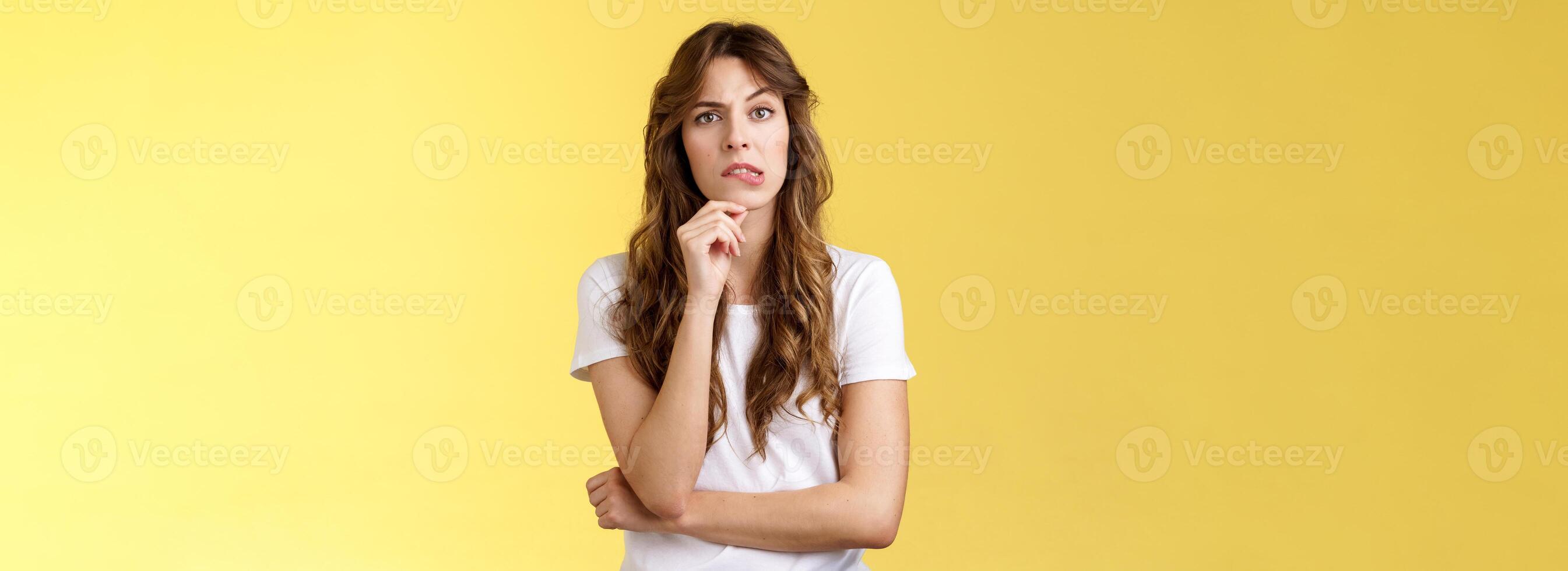 fastidioso situazione dare secondo pensare. incuriosito riflessivo focalizzata inteligente fidanzata pensiero toccare mento mordere labbro Guarda telecamera focalizzata meditando scelta fabbricazione decisione risolvere problema giallo sfondo foto