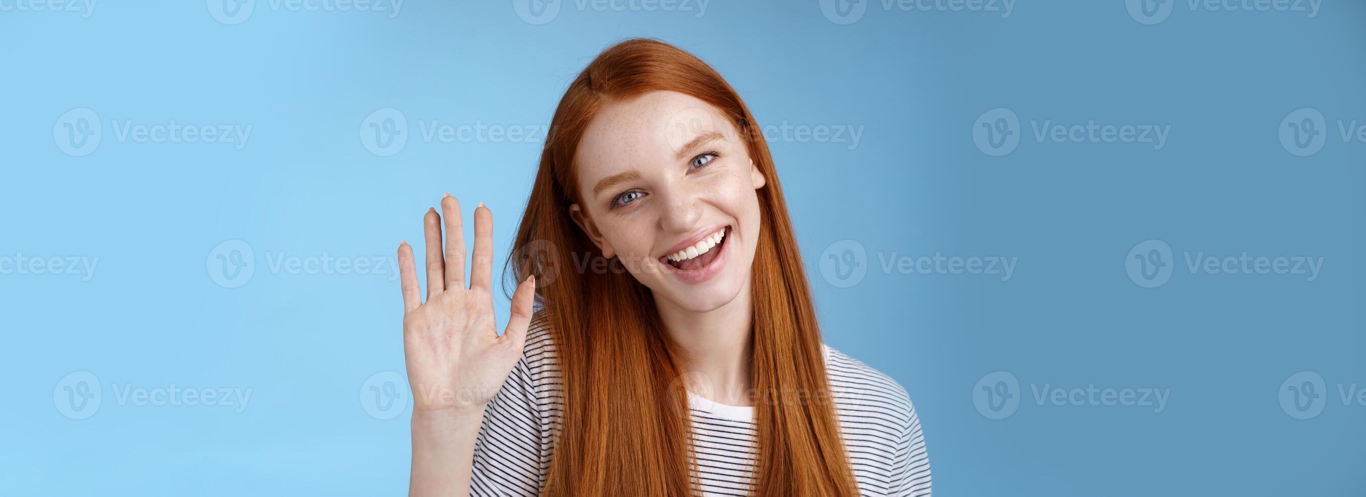 attraente fiducioso testa Rossa impertinente ragazza puro pulito pelle blu occhi ribaltamento testa allegramente agitando mano Ciao Ciao gesto saluto voi Guarda telecamera amichevole accogliente amico, in piedi studio sfondo foto