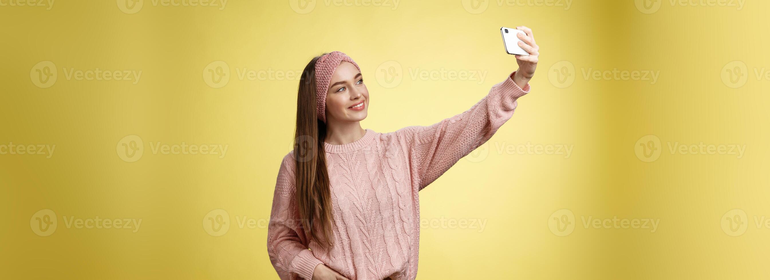popolare fascino giovane femmina Internet stile di vita blogger assunzione autoscatto su nuovo smartphone estendendosi braccio assunzione immagine se stessa contro giallo sfondo sorridente a cellulare schermo, in posa sfacciato foto