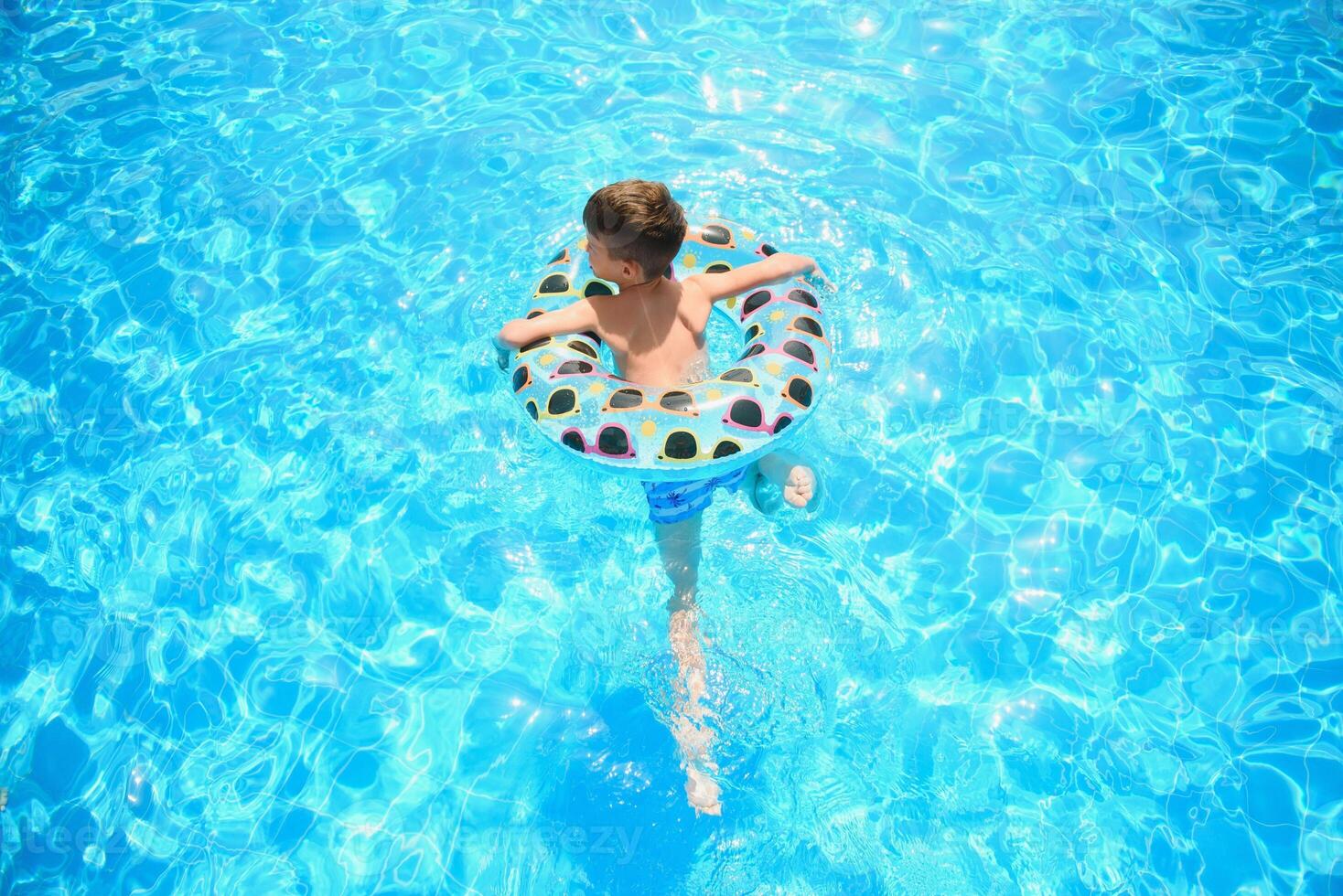 bambini estate vacanza. bambino nuoto nel piscina. bambini avendo divertimento a Parco acquatico. divertente ragazzo su gonfiabile gomma da cancellare cerchio. estate. attrazioni concetto foto