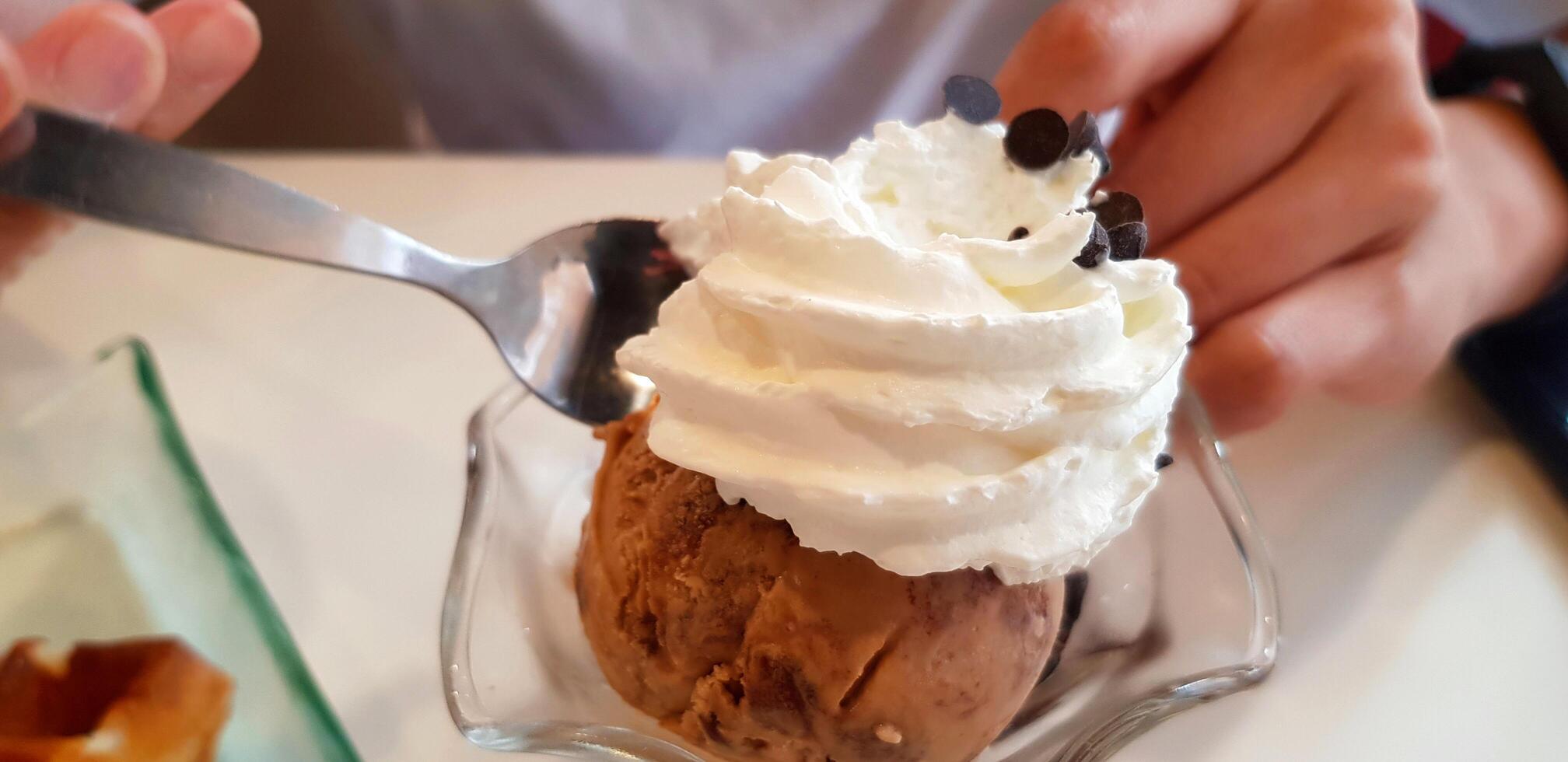 vicino su persone utilizzando cucchiaio per mangiare cioccolato ghiaccio crema con frustato crema su superiore. rinfresco e freddo o dolce cibo. foto