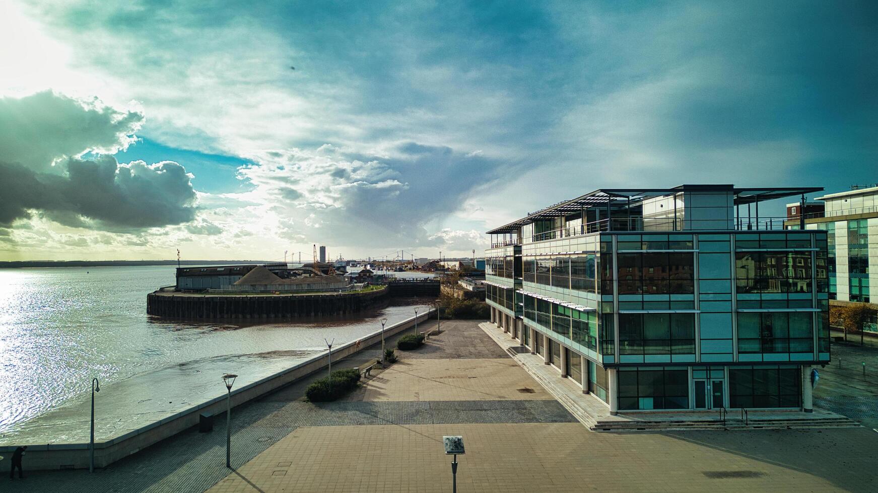 moderno lungomare ufficio edificio con bicchiere facciata sotto un' drammatico cielo, adiacente per un' calma fiume e un' attraccato barca nel scafo, Inghilterra. foto