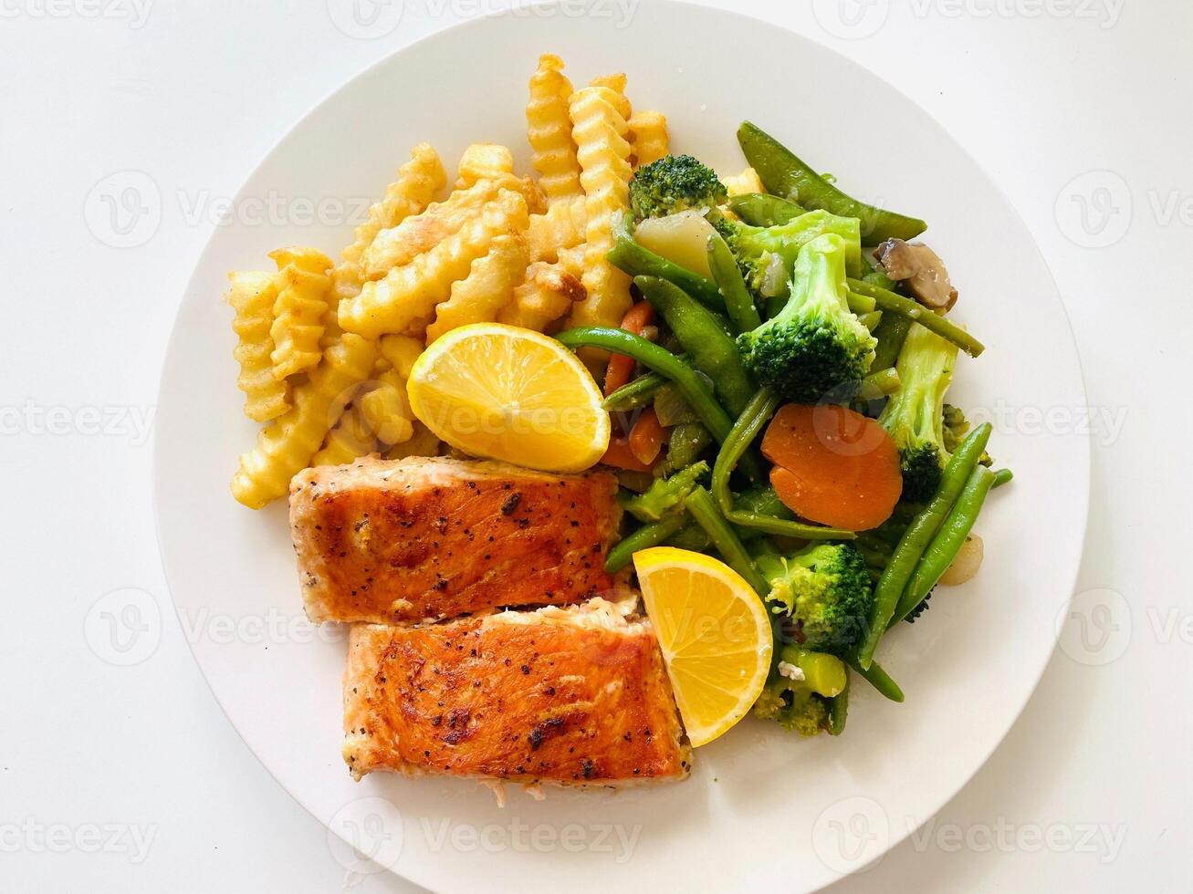 grigliato salmone con francese patatine fritte e verdure su un' bianca piatto. foto