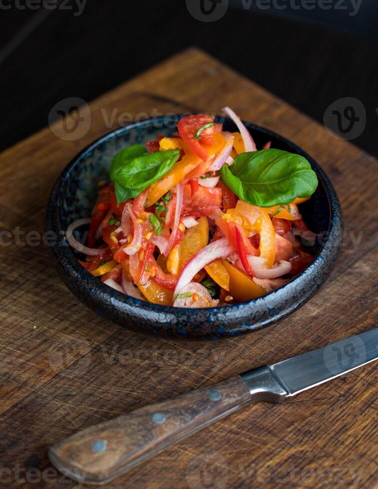 gustoso pomodoro insalata con cipolla e basilico nel nero ciotola su di legno tavolo foto