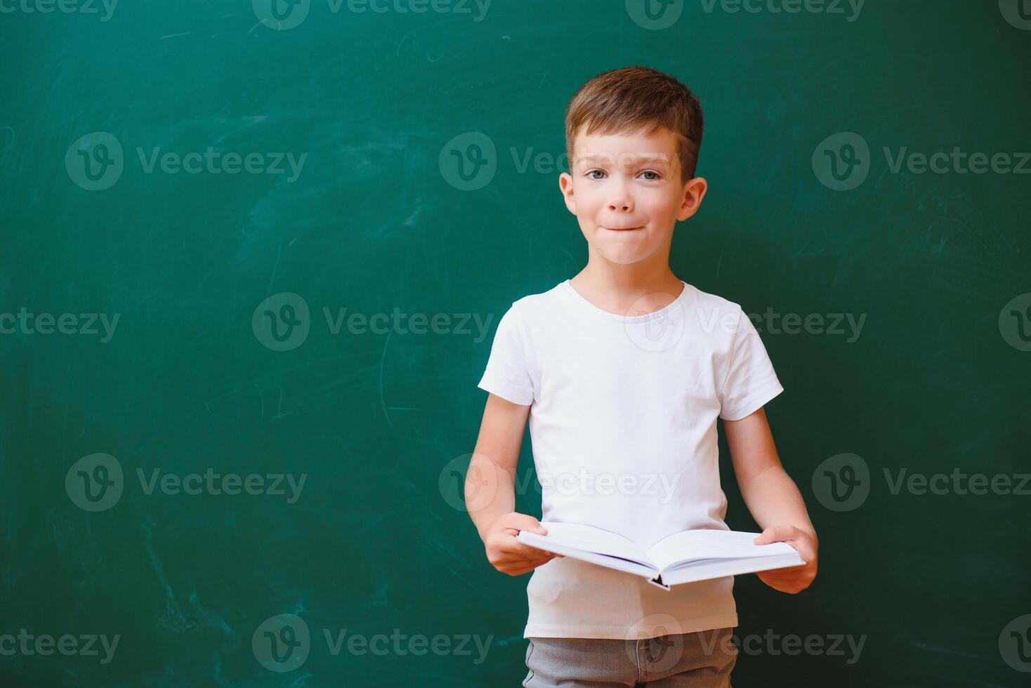 indietro per scuola concetto. scuola bambino nel classe. contento ragazzo contro verde lavagna. inteligente bambino nel aula. idea e formazione scolastica concetto foto