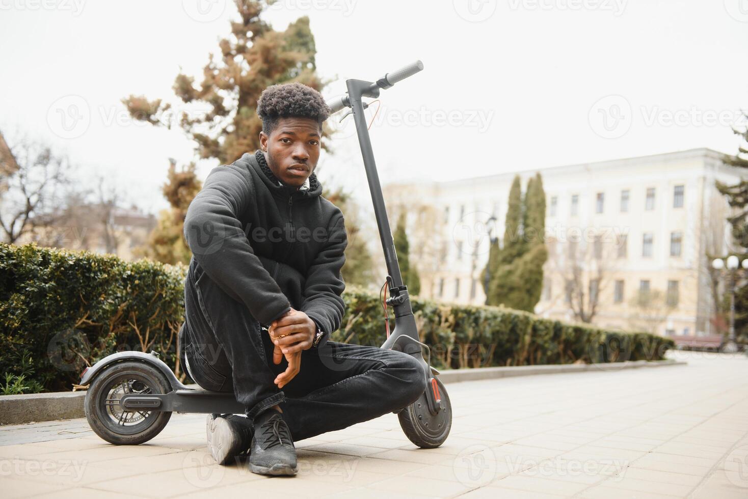 afro americano tipo cavalcate un elettrico scooter contro il sfondo di un' parete, un' alunno usi eco trasporto foto