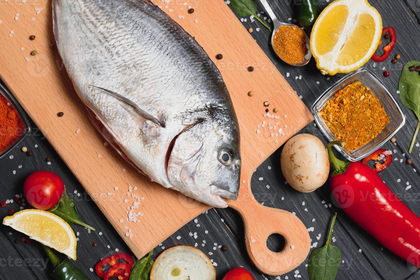 crudo mare pesce dorado con Limone, Pepe, pomodori e vario spezie. su un' nero rustico sfondo. foto