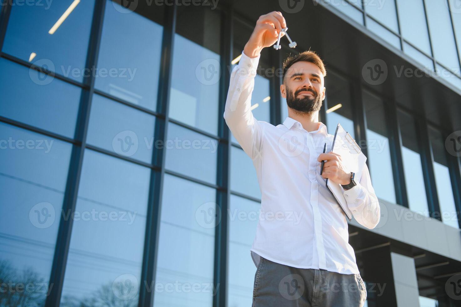 vero tenuta attraente agente bellissimo uomo con Casa chiavi nel davanti di venduto appartamento, nel città strada. giovane caucasico tipo nel bianca camicia con chiavi appena comprato nuovo appartamento. foto