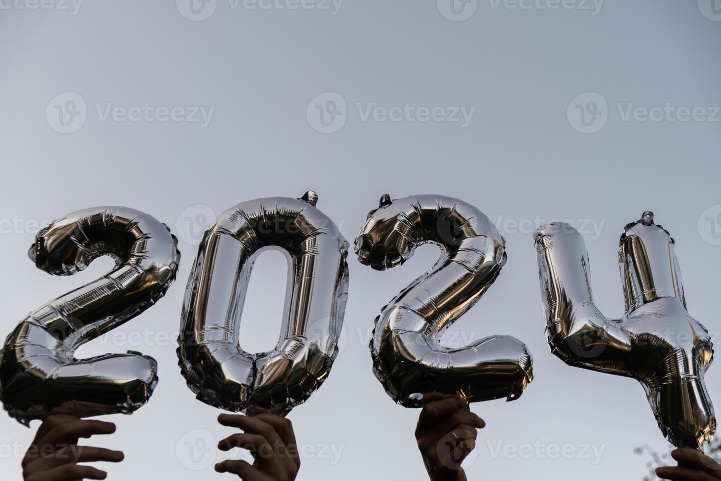 argento Foglio numero 2024 celebrazione nuovo anno Palloncino su blu cielo sfondo. contento nuovo anno saluti concetto. mani Tenere palloncini Due mille ventiquattresimo anno Natale vacanza concetto foto