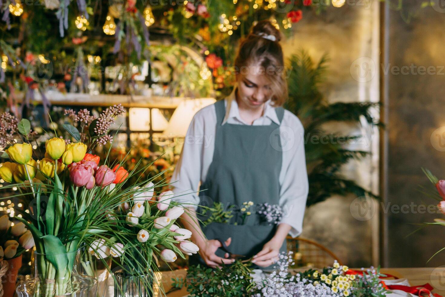 un' donna nel sua fioraio negozio raccoglie mazzi di fiori di fiori. il concetto di un' piccolo attività commerciale. mazzi di fiori di tulipani per il vacanza su marzo 8. foto