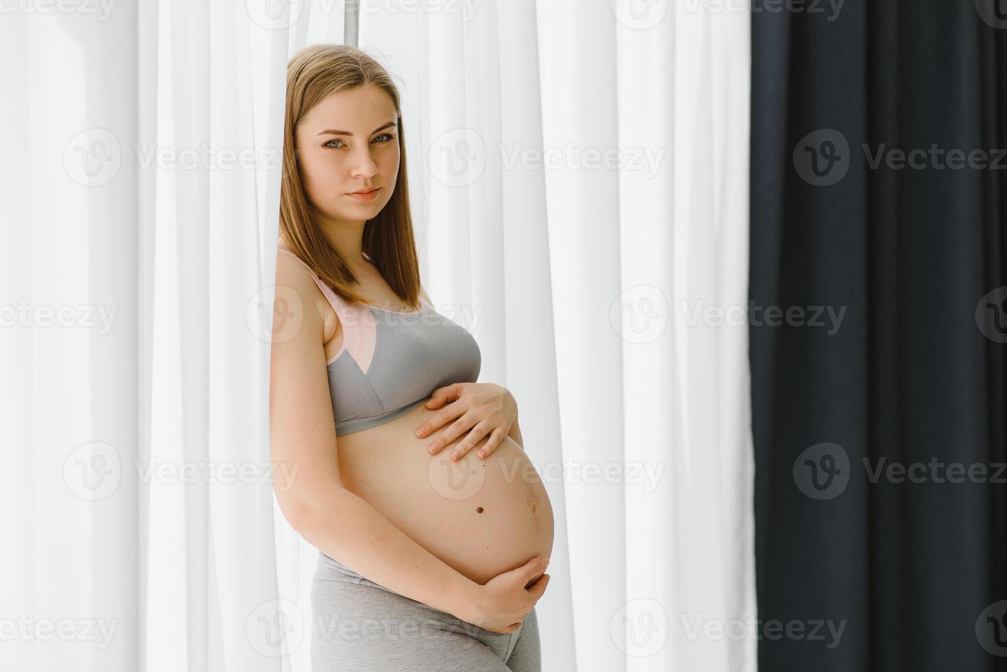 giovane bellissimo incinta donna in piedi a casa vicino il finestra. foto
