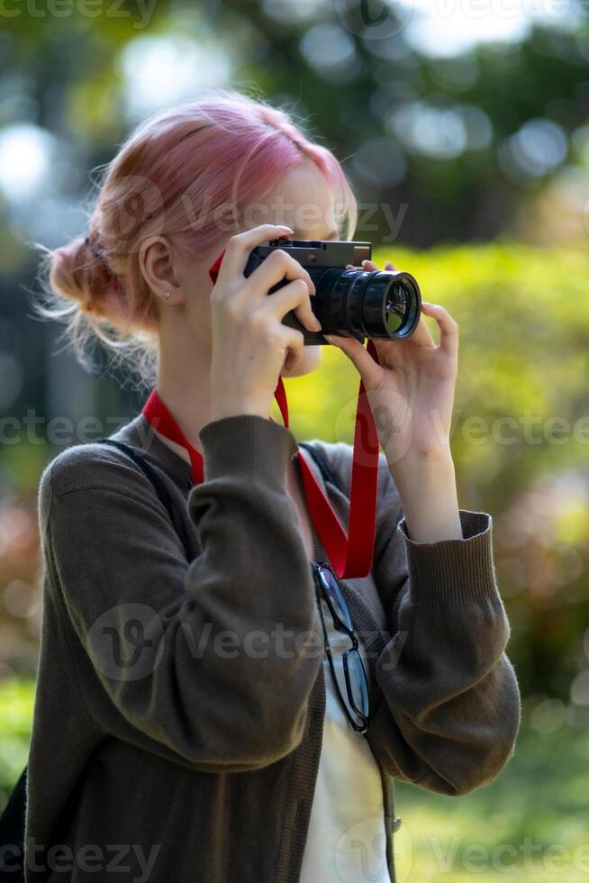 bellissimo giovane artista donna assunzione foto nel fiori giardino. giovane carino ragazza trasportare il telecamera nel il giardino