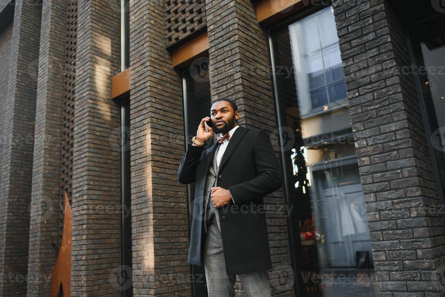 attività commerciale comunicazioni. contento giovane africano uomo nel formale indossare parlando su il mobile Telefono e sorridente mentre in piedi all'aperto foto