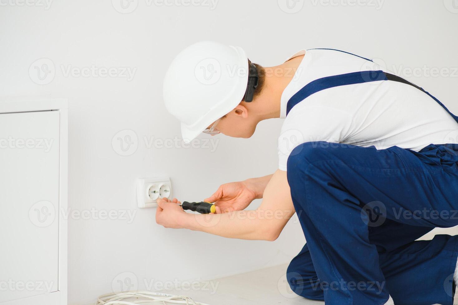 un' giovane elettricista installazione un elettrico presa di corrente nel un' nuovo Casa. foto
