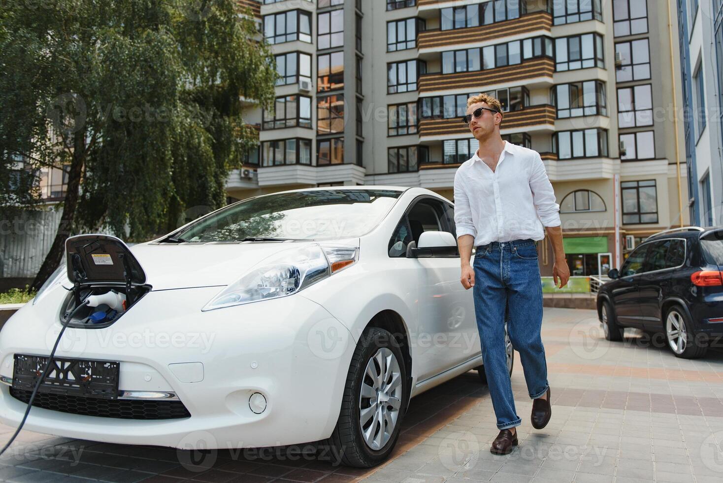 ritratto di giovane bello uomo nel casuale indossare, in piedi a il ricarica stazione. eco elettrico auto concetto foto