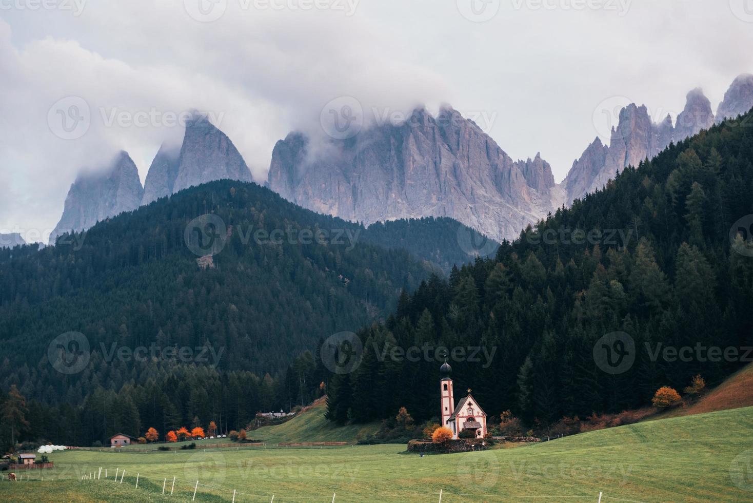 giornata nuvolosa. fattoria con cappella vicino al bosco. maestose montagne sullo sfondo foto