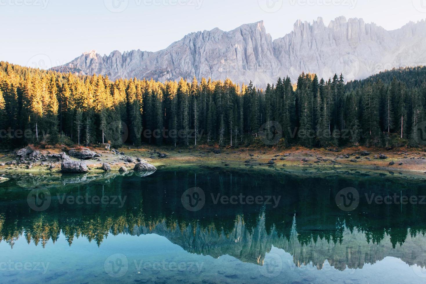 paesaggio autunnale con lago limpido, bosco di abeti e montagne maestose foto