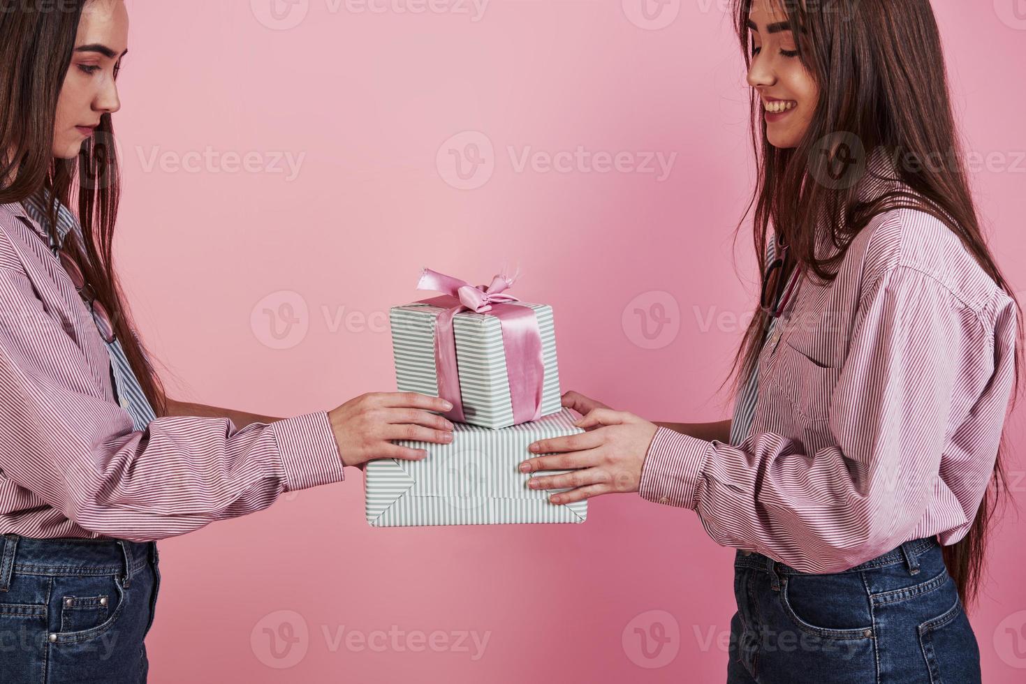 vista laterale. foto ravvicinata di due ragazze che tengono scatole regalo su sfondo rosa in studio