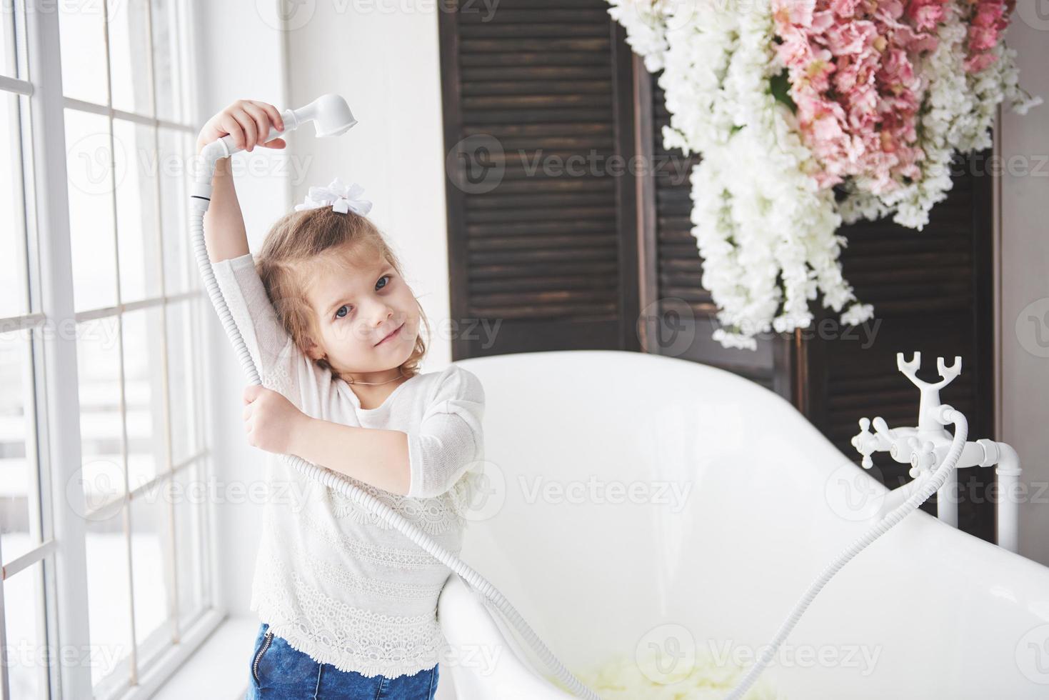 piccola neonata divertente con capelli ricci. preparati a fare il bagno. ampio bagno illuminato. il concetto di un corpo sano e pulito. prendersi cura di sé fin dall'infanzia foto