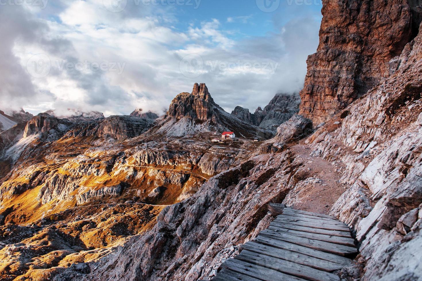 luci del sole che attraversano le nuvole. percorso turistico estremo ai margini delle colline con ponticello in legno per la via dell'edificio in piedi sulle montagne dolomitiche foto