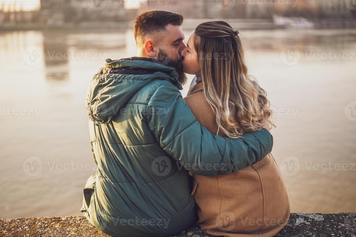 contento coppia baci e Abbracciare una persona mentre godere seduta di il fiume. foto