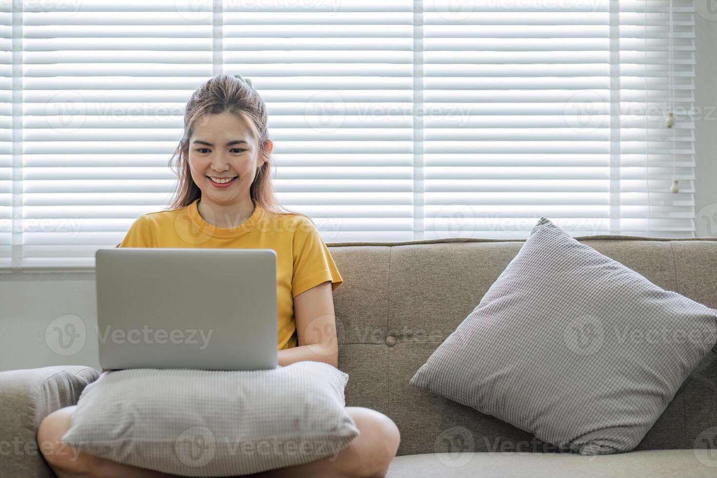 bellissimo asiatico donna indossare casuale Abiti su il divano utilizzando un' il computer portatile computer, divertente con sociale media, rilassante, sorridente e ridendo. foto