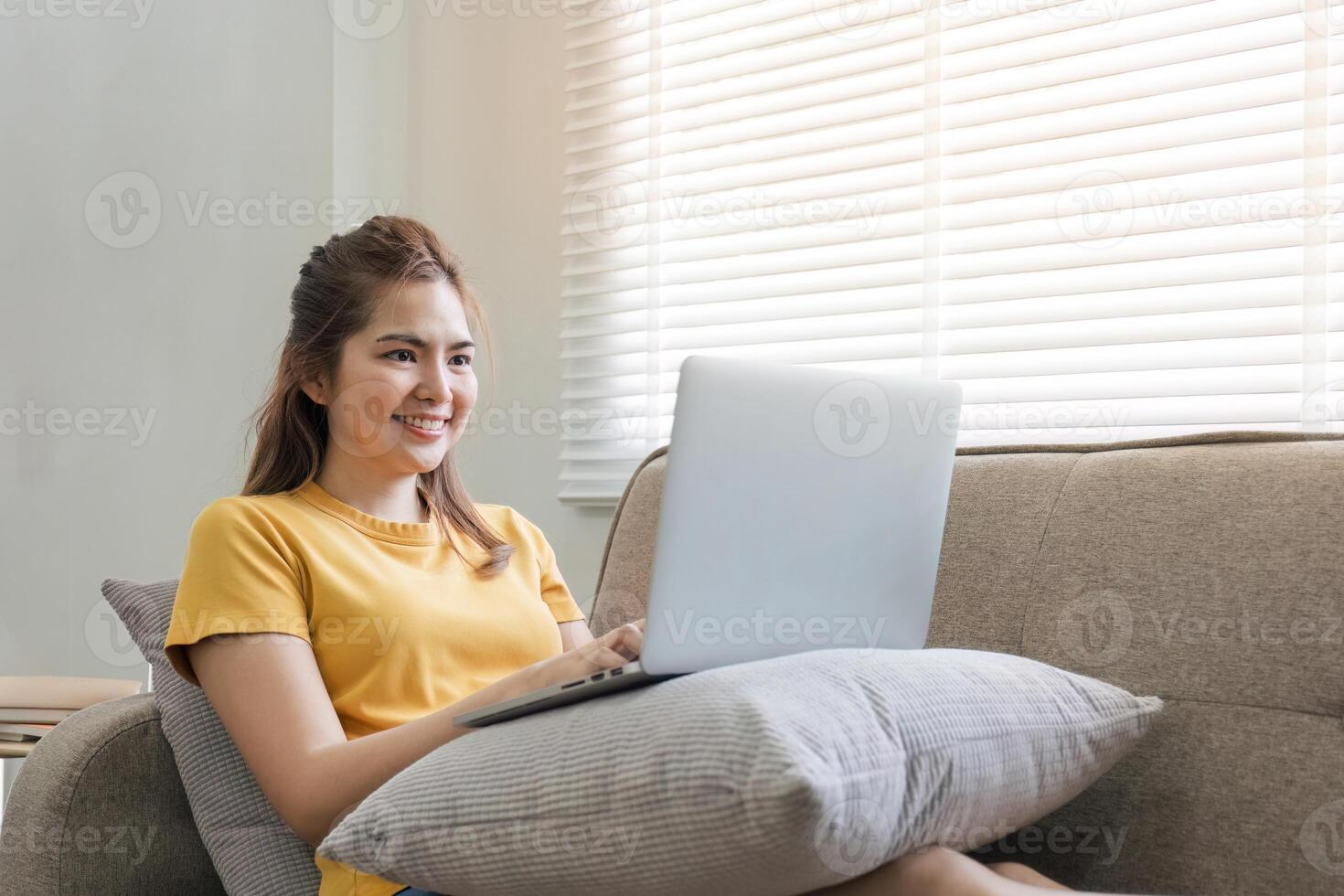 bellissimo asiatico donna indossare casuale Abiti su il divano utilizzando un' il computer portatile computer, divertente con sociale media, rilassante, sorridente e ridendo. foto