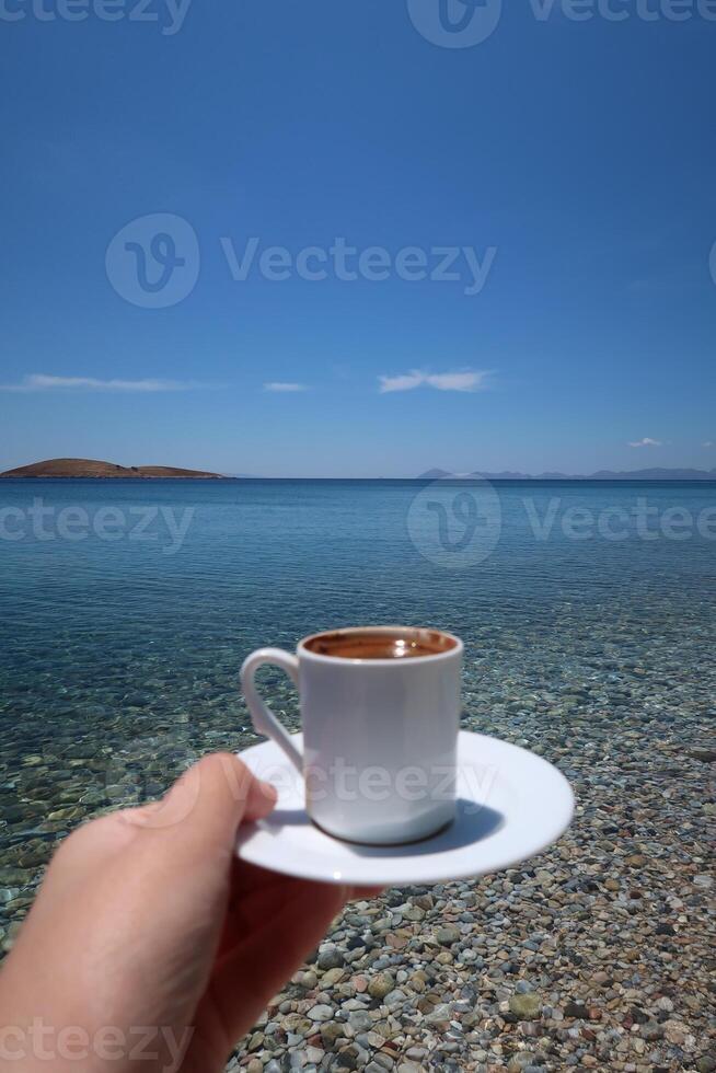 tradizionale Turco caffè tazza con modelli. donna mano Tenere il tazza su un' soleggiato estate giorno, esotico mare sfondo foto