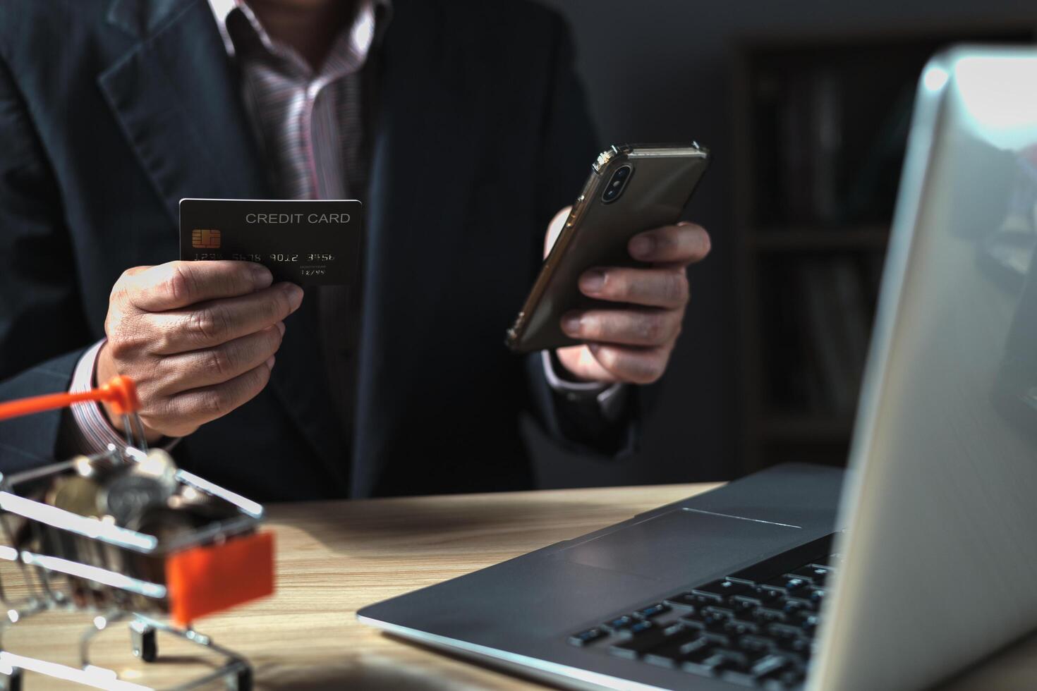 uomo d'affari usi un' computer il computer portatile e credito carta per acquistare o Acquista produrre pagamento in linea e si siede su il sedia nel il vivente camera a casa. il concetto di finanza e in linea acquisti. foto