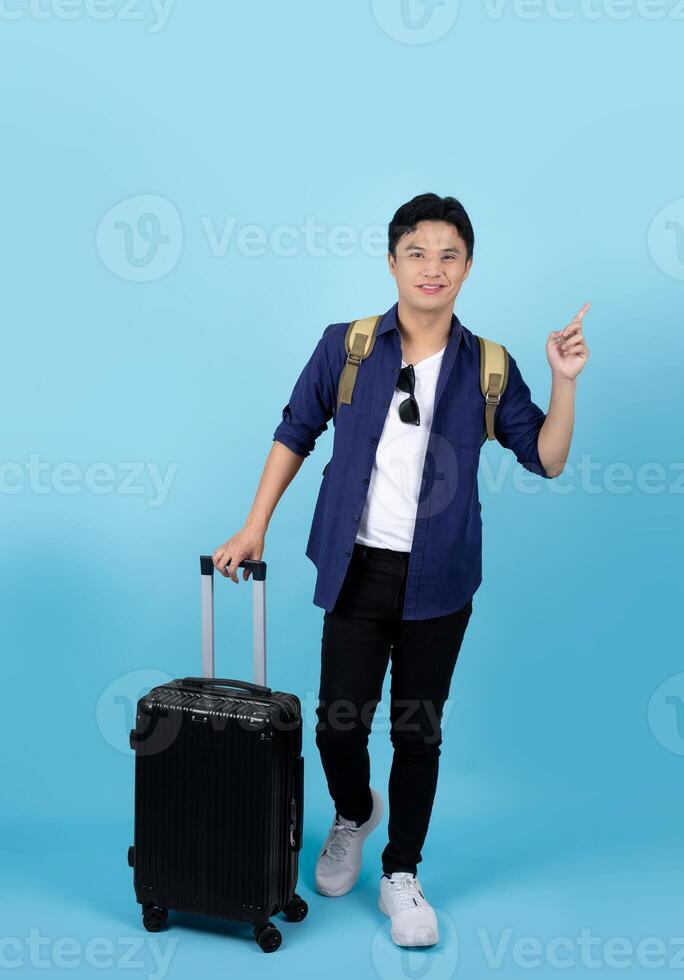 pieno corpo viaggiatore uomo di asiatico etnia indossare casuale Abiti hold valigia valigetta isolato su pastello blu sfondo. foto
