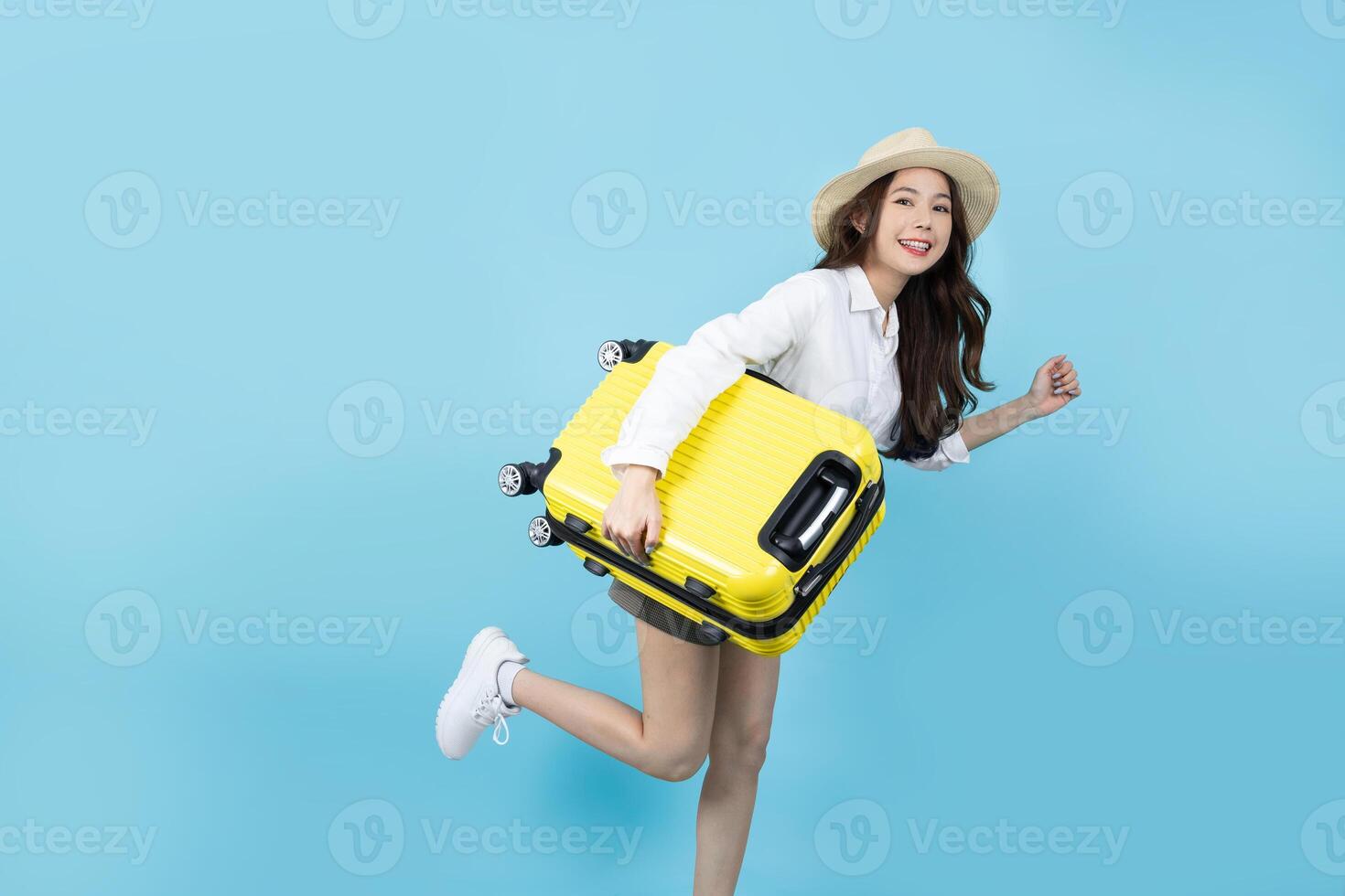 contento asiatico femmina viaggiatore in piedi e Tenere un' valigia isolato su blu sfondo. turista ragazza pronto per viaggio per un' vacanza viaggio. foto