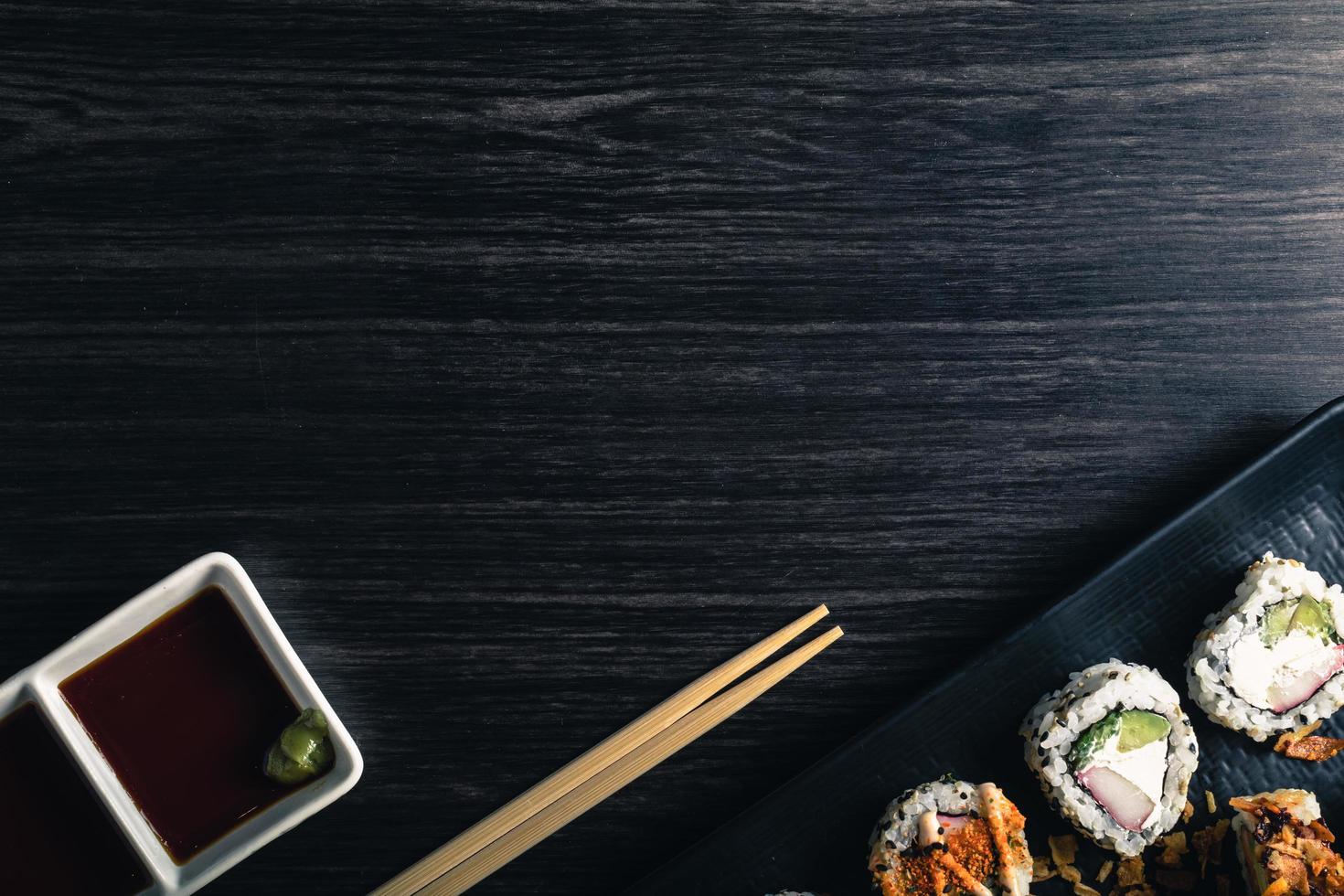 rotoli di sushi con le bacchette e salsa di soia su sfondo scuro. spazio testo foto