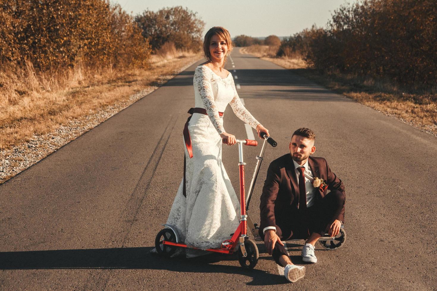 sposi sorridenti in sella a uno scooter lungo la strada fuori città al tramonto. foto