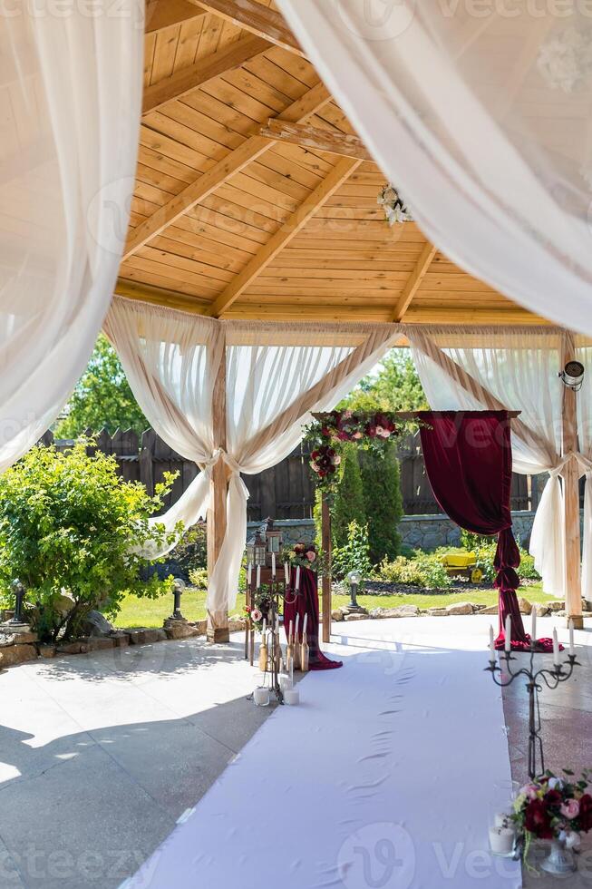 decorativo arco per il nozze cerimonia di il Novelli sposi. Borgogna le tende e bellissimo fiori. foto