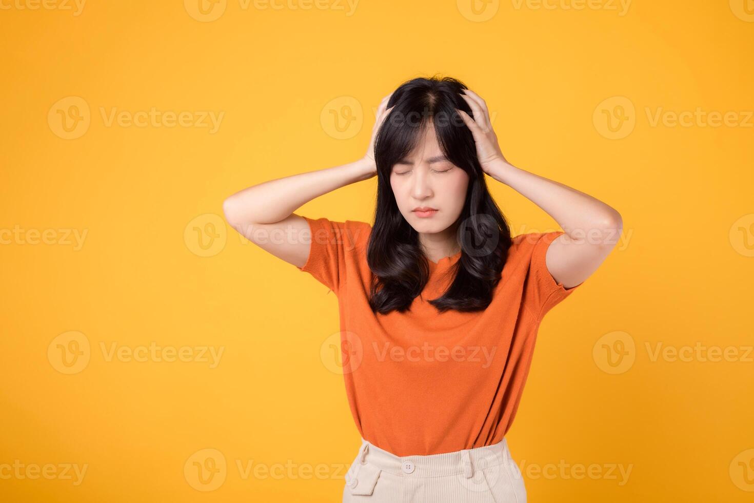 espressive ritratto di un' giovane asiatico donna 30s nel angoscia, in piedi nel un' giallo studio sfondo, illustrare fatica, male alla testa, e Salute preoccupazioni. foto
