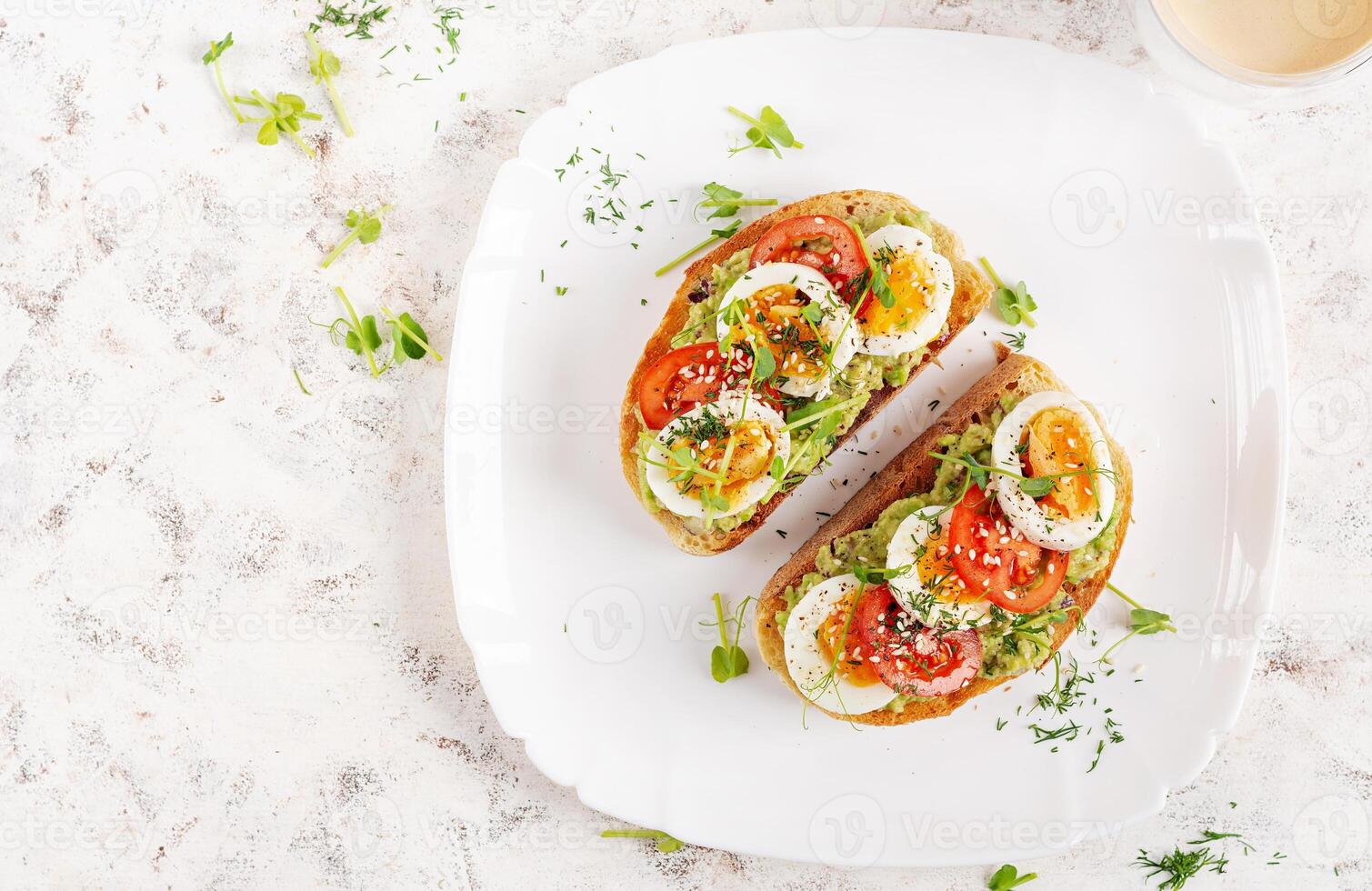 delizioso crostini con avocado, bollito uovo, pomodori e microgreen su un' bianca piatto. salutare mangiare, prima colazione. cheto dieta cibo. di moda cibo. superiore Visualizza foto