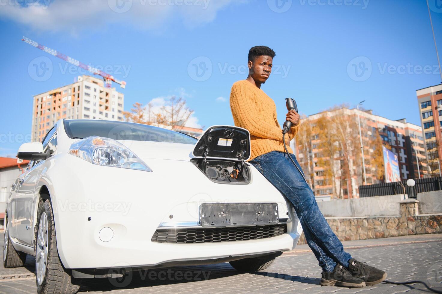 elettrico macchine, ev concetto, eco amichevole carburante. ritratto di giovane sorridente nero uomo, ricarica il suo moderno lusso elettrico auto foto