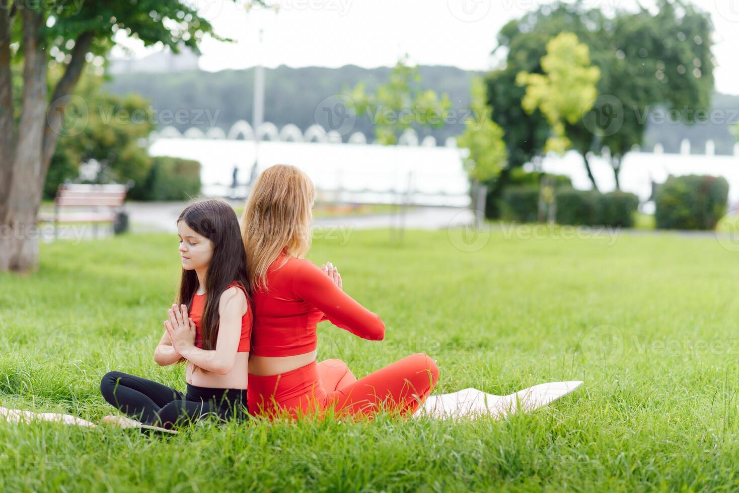 madre e figlia fare yoga esercizi su erba nel il parco a il giorno volta. persone avendo divertimento all'aperto. concetto di amichevole famiglia e di estate vacanza. foto
