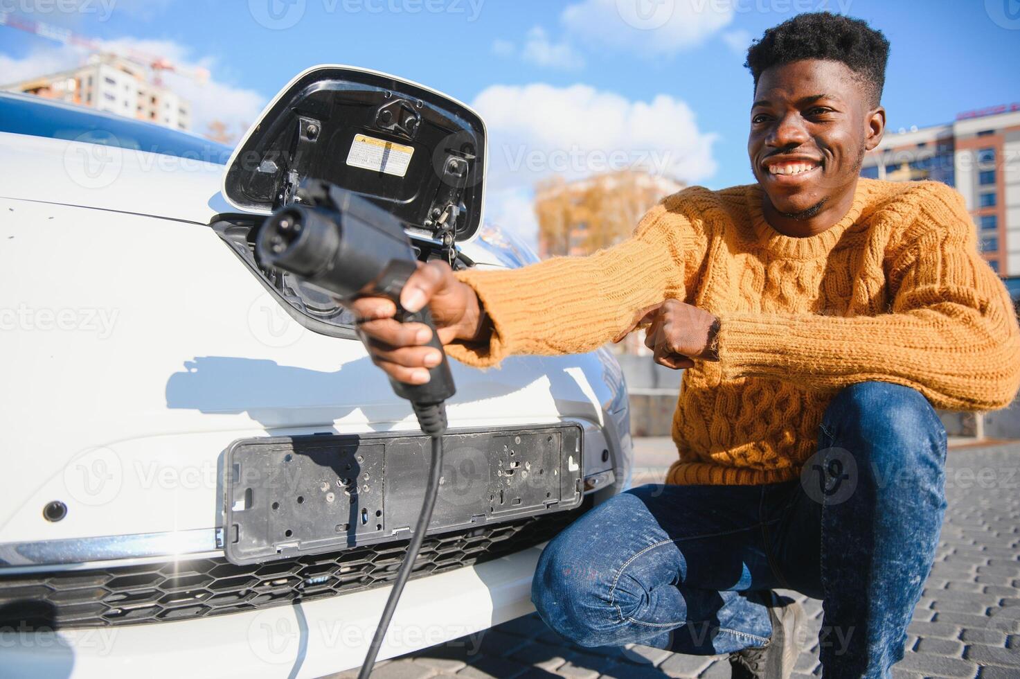 elettrico macchine, ev concetto, eco amichevole carburante. ritratto di giovane sorridente nero uomo, ricarica il suo moderno lusso elettrico auto foto