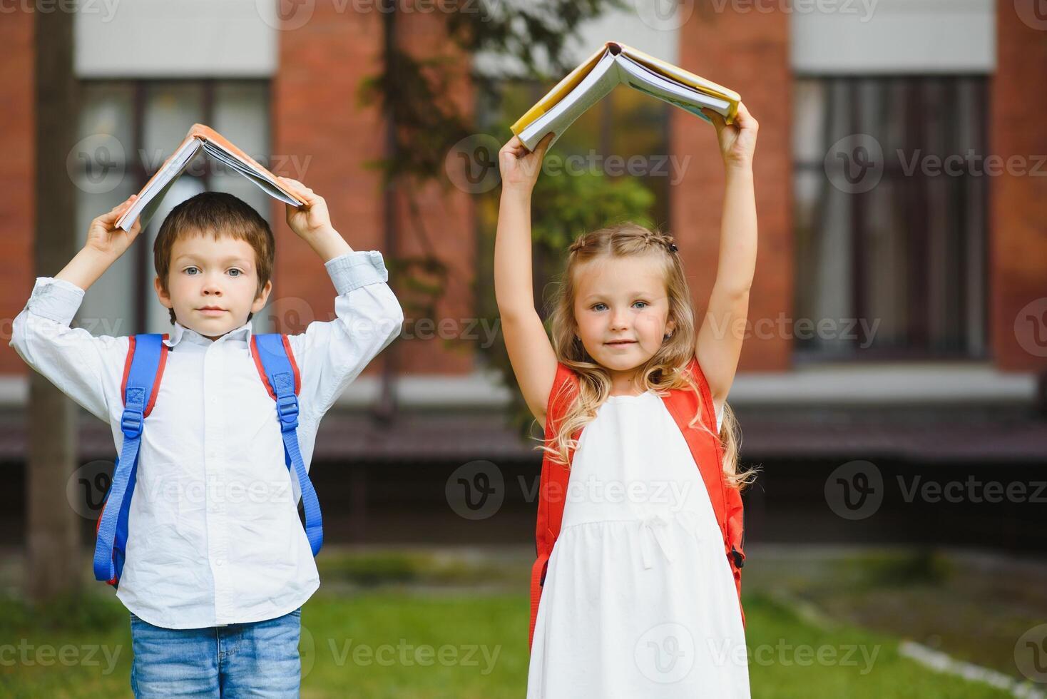 contento bambini - ragazzo e ragazza con libri e zaini su il primo scuola giorno. eccitato per essere indietro per scuola dopo vacanza. pieno lunghezza all'aperto ritratto. foto