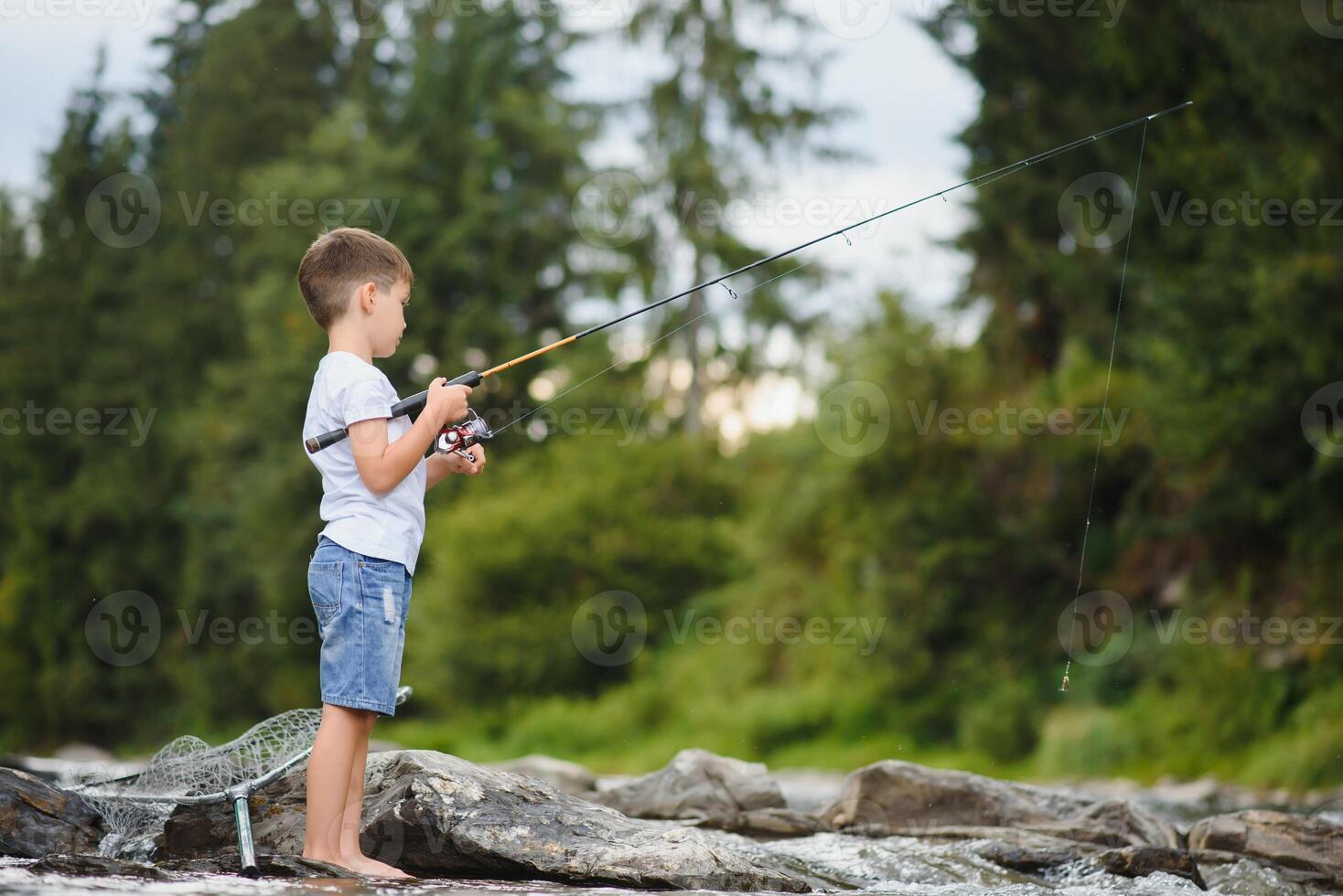 carino ragazzo nel bianca t camicia pesca nel il fiume e ha divertimento, sorrisi. vacanza con bambini, vacanze, attivo fine settimana concetto foto