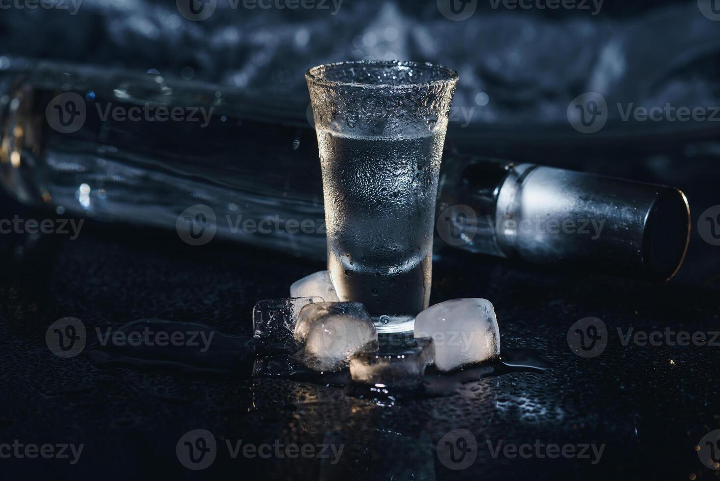 avvicinamento Visualizza di bottiglia di Vodka con bicchieri in piedi su ghiaccio su nero. foto
