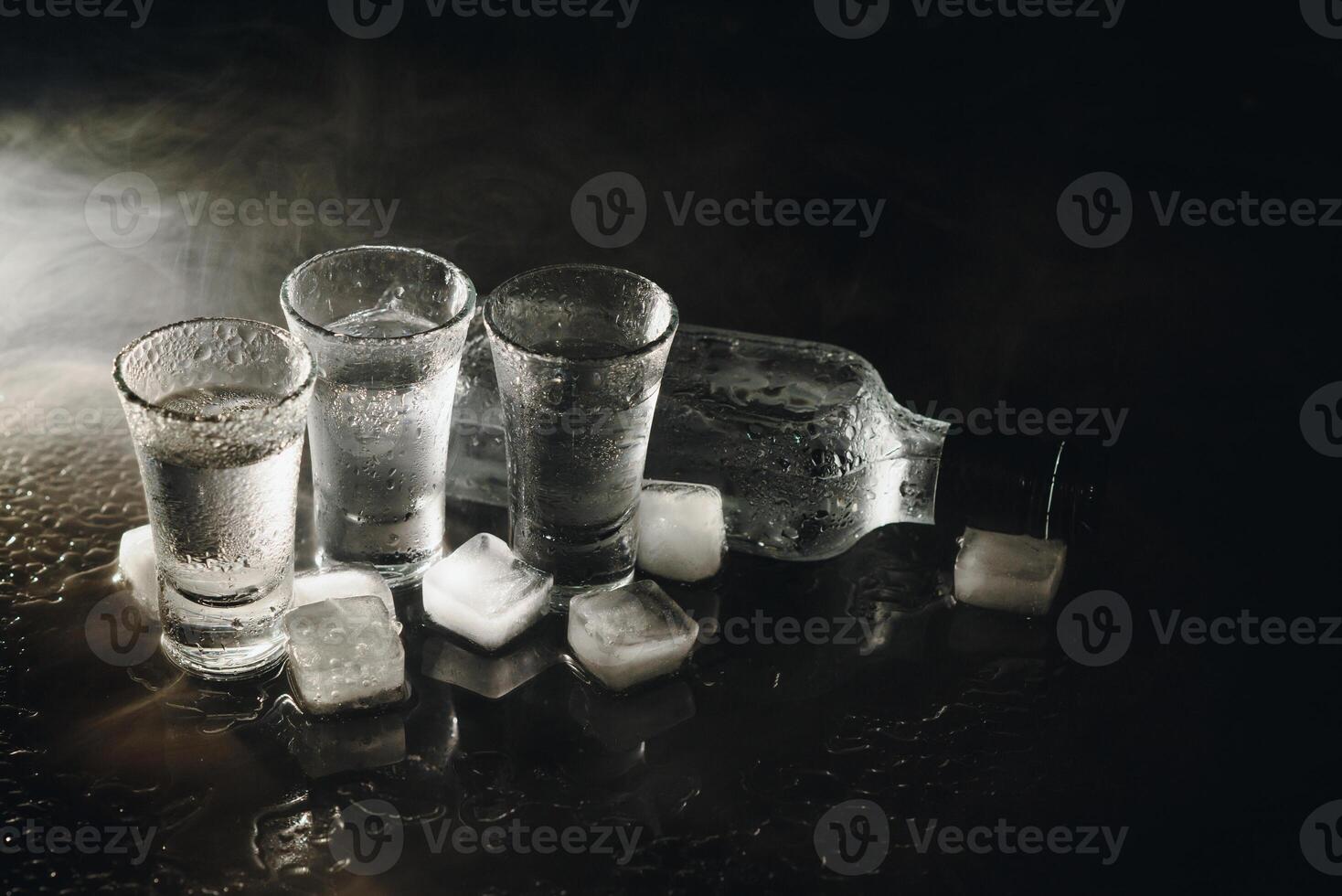 avvicinamento Visualizza di bottiglia di Vodka con bicchieri in piedi su ghiaccio su nero. foto