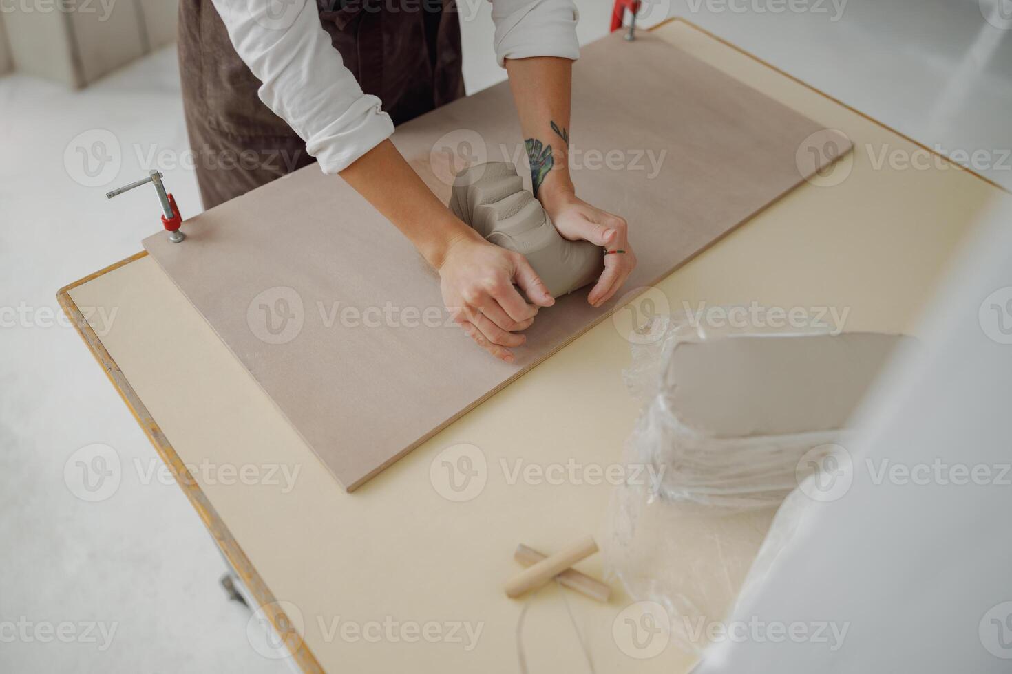 vicino su di femmina vasaio nel grembiule impasta pezzo di argilla con sua mani su tavolo nel studio foto