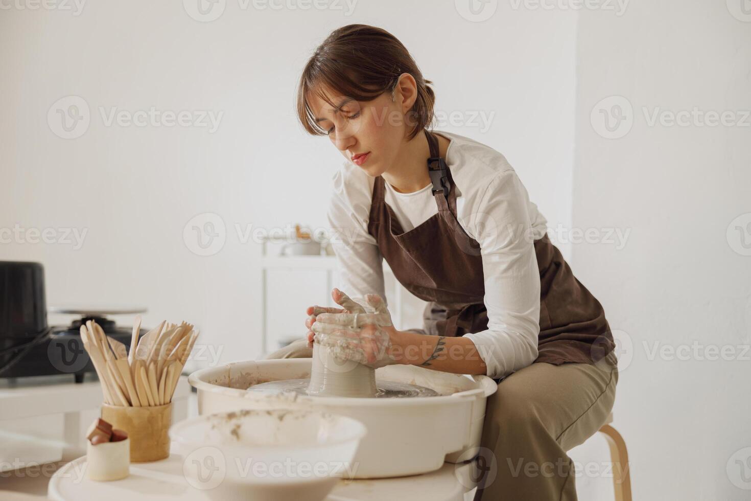 concentrato femmina artigiano nel grembiule seduta su panchina con ceramica ruota e fabbricazione argilla pentola foto