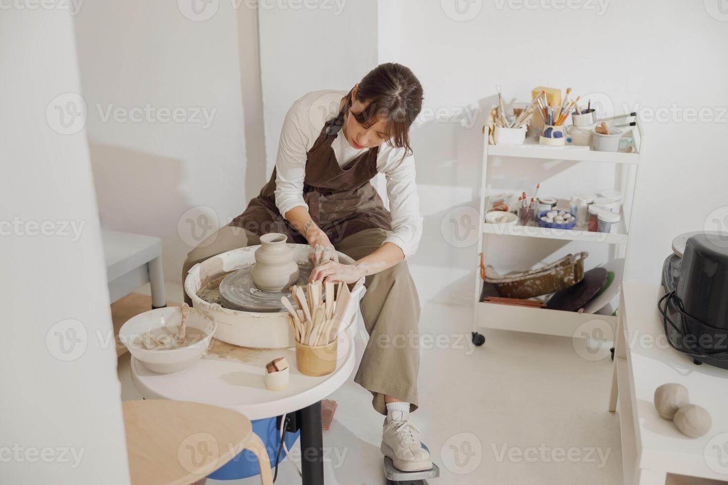 focalizzata femmina artigiano nel grembiule seduta su panchina con ceramica ruota e fabbricazione argilla pentola foto