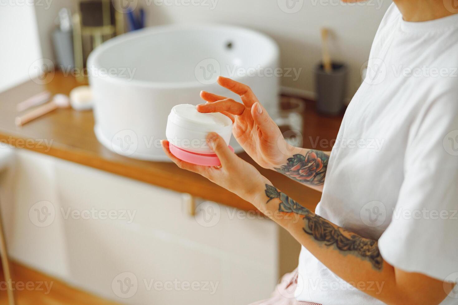 vicino su di donna apertura vaso con viso crema mentre in piedi nel bagno. alto qualità foto